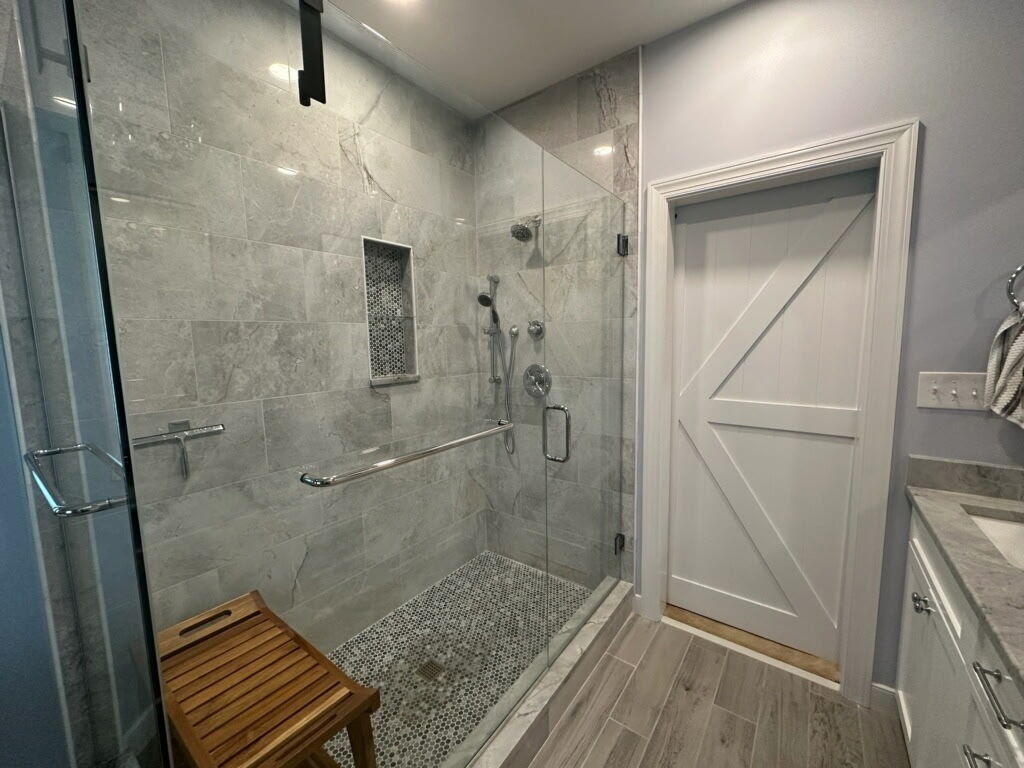 Luxury walk-in shower with polished porcelain walls, penny round niche, frameless glass door, and chrome Delta fixtures.